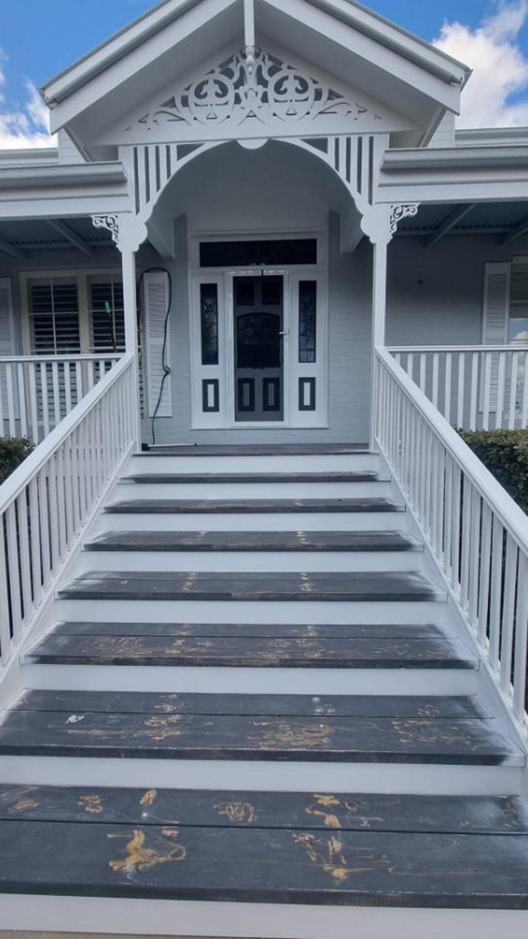 Worn, patchy front stair treads below a house entrance with white fretwork