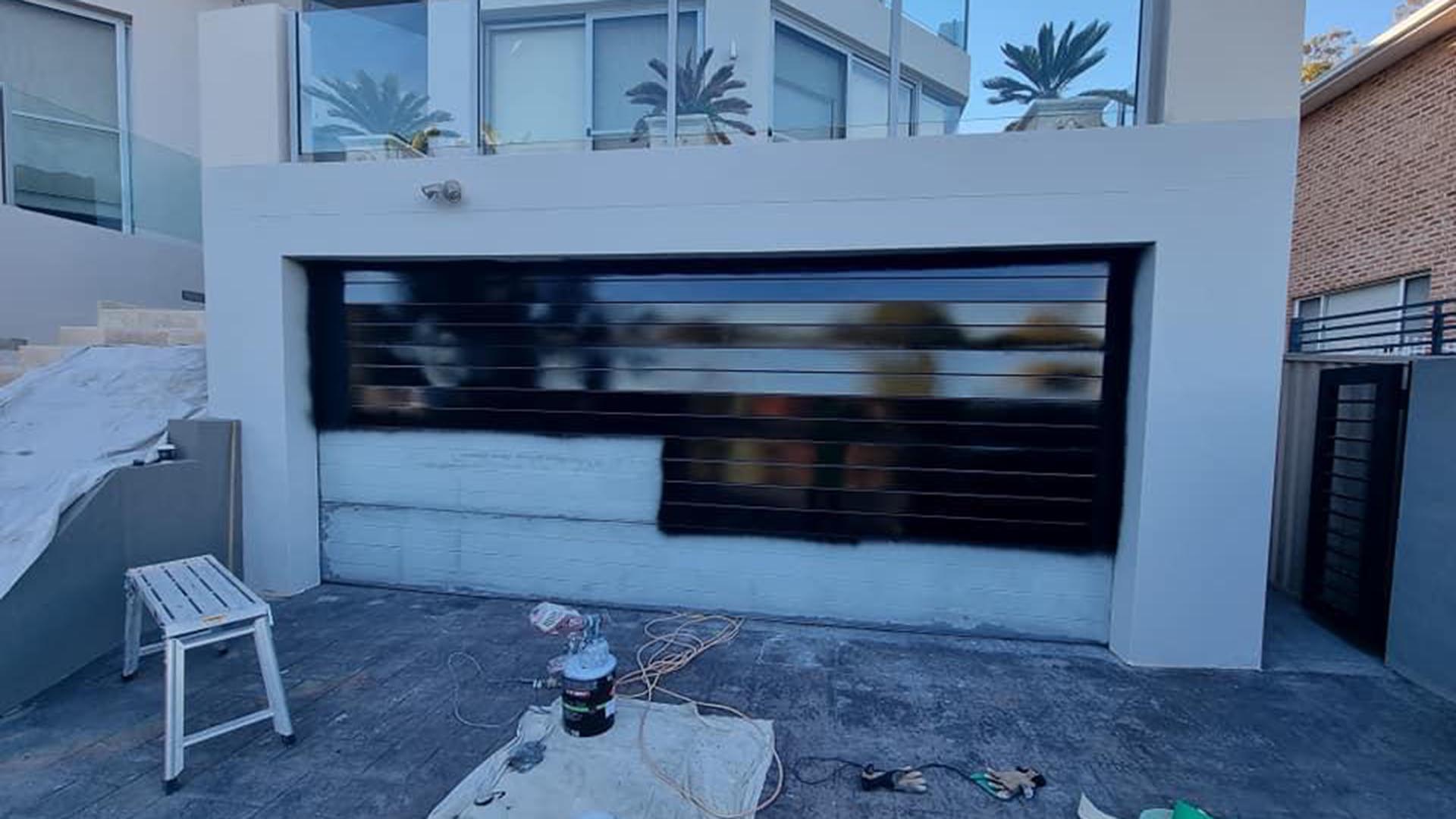 Garage door partly painted black, lower panels still white